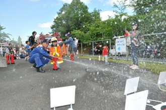 写真：ヘルメットと消防服を着て水消火器を使って消火体験をするこどもの様子