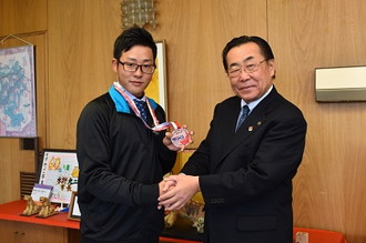 写真：メダルを見せる渡邉さんと水野市長が握手する様子