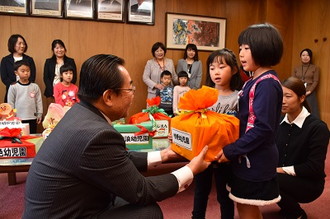 写真：丁寧にラッピングされた募金の箱を、市長に手渡す園児と、屈んで受け取る市長