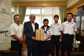 写真：義援金をもって並ぶ日比野昭会長と生徒会の3人と男性