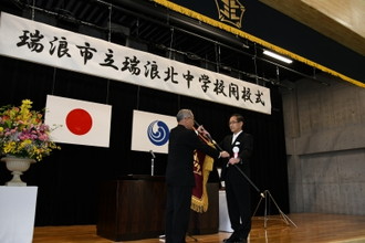 写真：平林道博教育長から安藤雅哉校長への校旗授与の様子