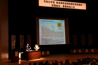 写真：定期総会及び事業推進大会で壇上で説明をしている男性