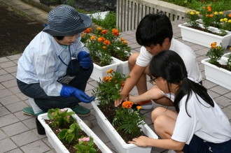 写真：オレンジの花を植える人権擁護委員と二人の子どもたち