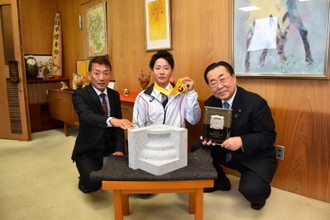 写真：金賞の盾・受賞作品とともに、金メダルを手に男性二人と並ぶ渡邉龍さん