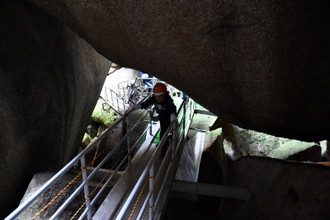 写真：大きな岩の下を手すりにつかまりながら進む参加者の様子