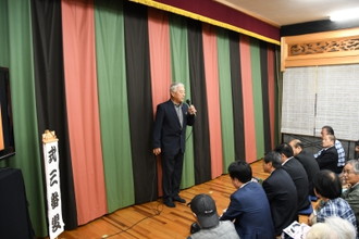 写真：式三番叟と演目の書かれた横で司会をする男性