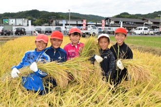 写真：束ねた稲を抱えている笑顔の子どもたちの様子