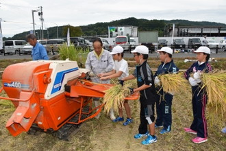 写真：稲の束を持って脱穀機に並ぶ子どもたちの様子