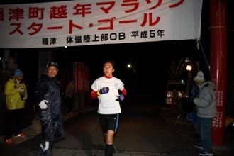 写真：稲津町越年マラソン　スタート・ゴールと書いてある横断幕の下を走り抜ける参加者の様子