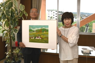 写真：寄贈された「隠し絵」のうちの1枚を手に記念写真を撮る、中山さんと教育長
