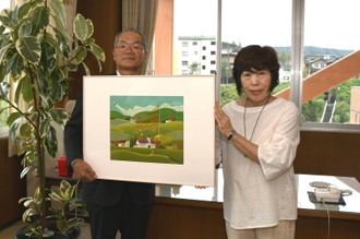 写真：寄贈された「隠し絵」のうちの1枚を手に記念写真を撮る、中山さんと教育長