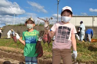 写真：男の子2人が堀ったサツマイモを持ち上げている様子