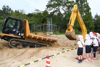 写真：トラックに土砂を積み込む様子を見る児童